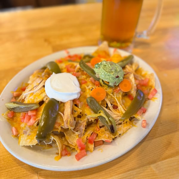 A plate of chicken nachos with cheese, tomatoes, jalapeños, sour cream, and guacamole, with a beer.