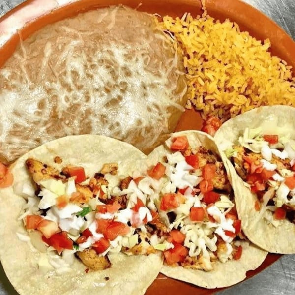 Three chicken tacos with diced tomatoes, shredded lettuce, and sour cream, alongside rice and refried beans.