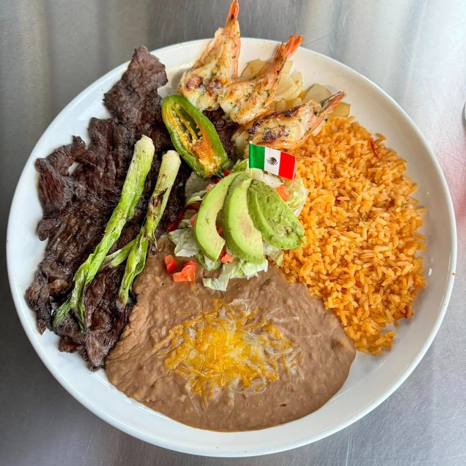 A Mexican dish with grilled steak, shrimp, rice, refried beans, avocado, and a Mexican flag pick.