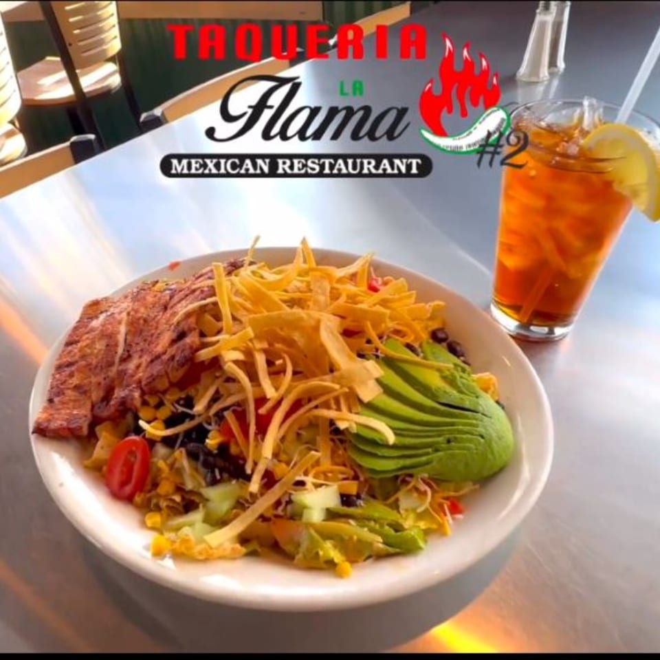 A vibrant Mexican salad with grilled chicken, avocado, tortilla strips, and a glass of iced tea.