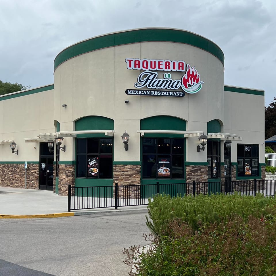 Exterior of Taqueria La Flama Mexican Restaurant with a curved facade, green trim, and stone accents.