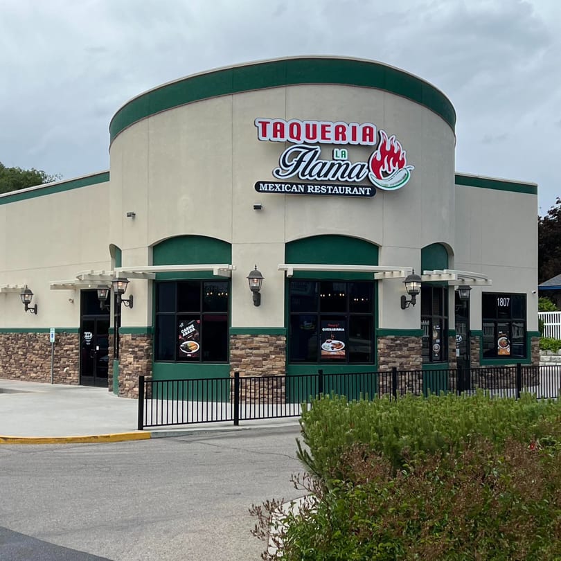 Exterior of Taqueria La Flama Mexican Restaurant with a curved facade, green trim, and stone accents.