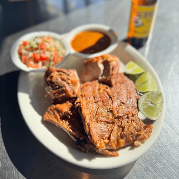 Mexican carnitas with lime wedges, pico de gallo, and salsa, alongside a beer bottle.