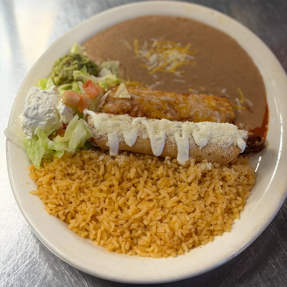 Mexican combination plate with rice, refried beans, enchilada, taquito, guacamole, sour cream, and salad.