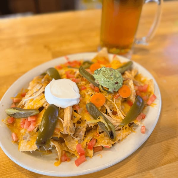 Chicken nachos with melted cheese, jalapeños, tomatoes, sour cream, and guacamole, with a beer.