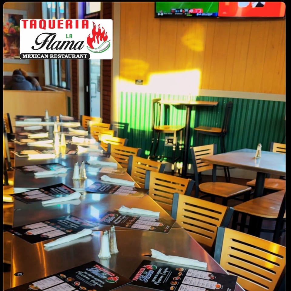 Interior of Taqueria La Flama Mexican Restaurant with empty tables, chairs, and menus, bathed in sunlight.