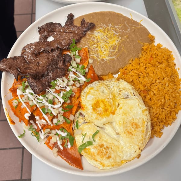 A Mexican breakfast plate with carne asada, chilaquiles, refried beans, rice, and fried eggs.