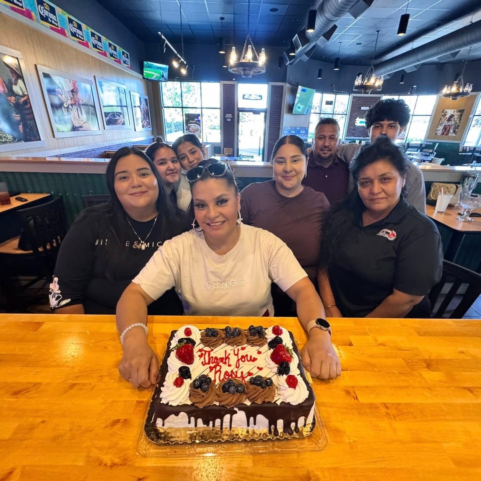 Group of people smiling around a "Thank You Rosy" cake at Taqueria La Flama.