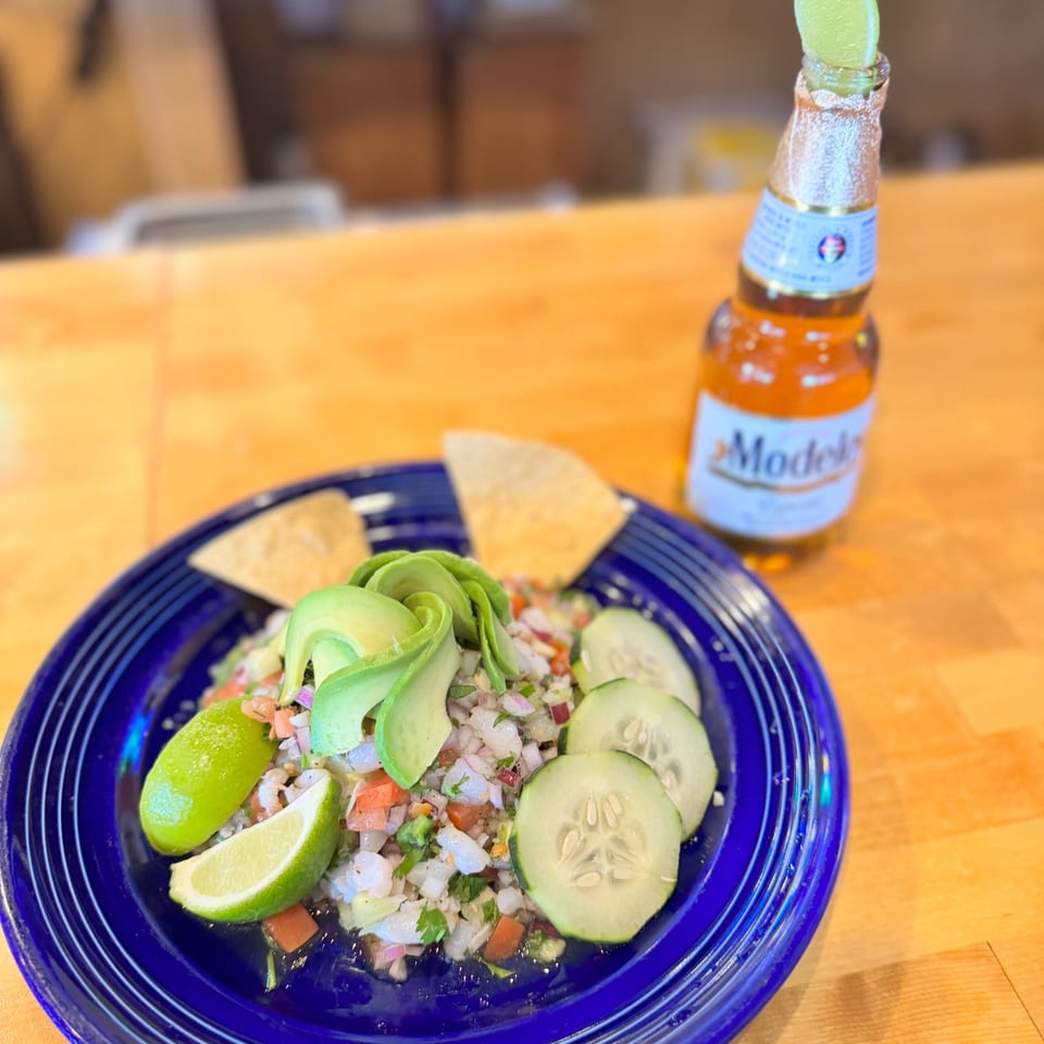 Ceviche with avocado, cucumber, and lime on a blue plate, with tortilla chips and a Modelo beer.