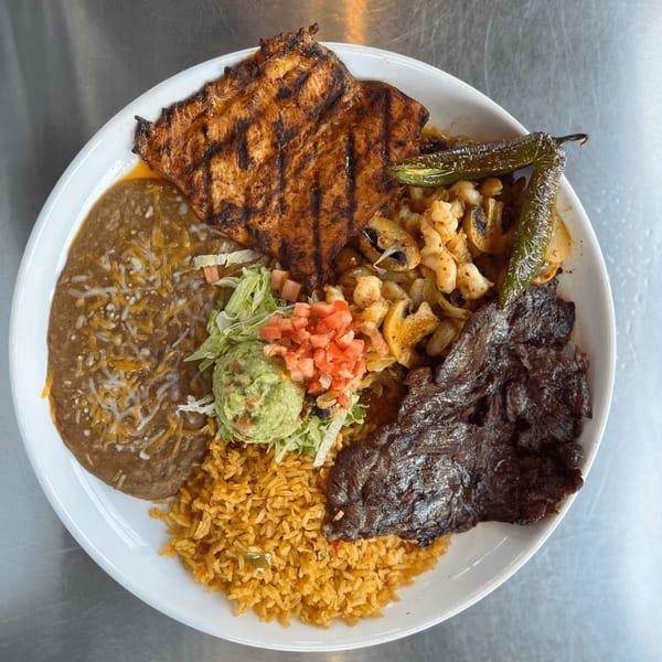 A Mexican platter with grilled chicken, steak, rice, refried beans, guacamole, and grilled peppers.