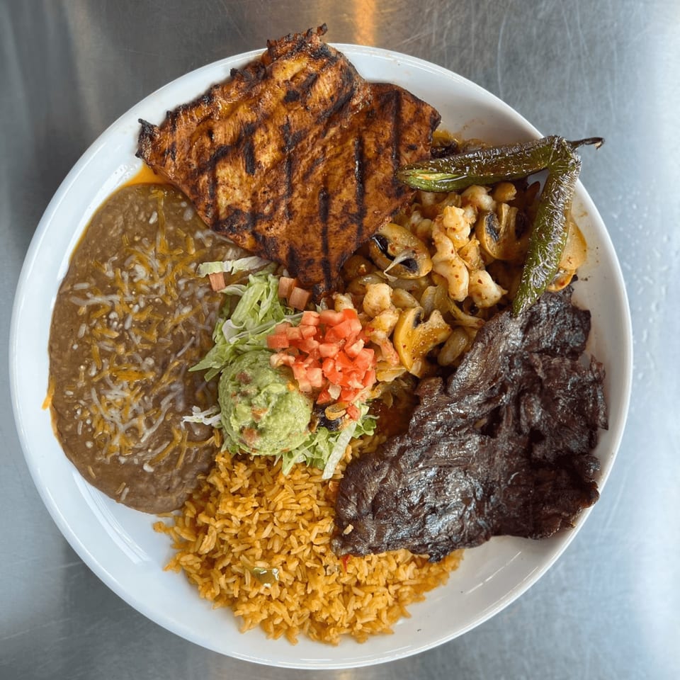 A Mexican platter with grilled chicken, steak, rice, refried beans, guacamole, and grilled peppers.