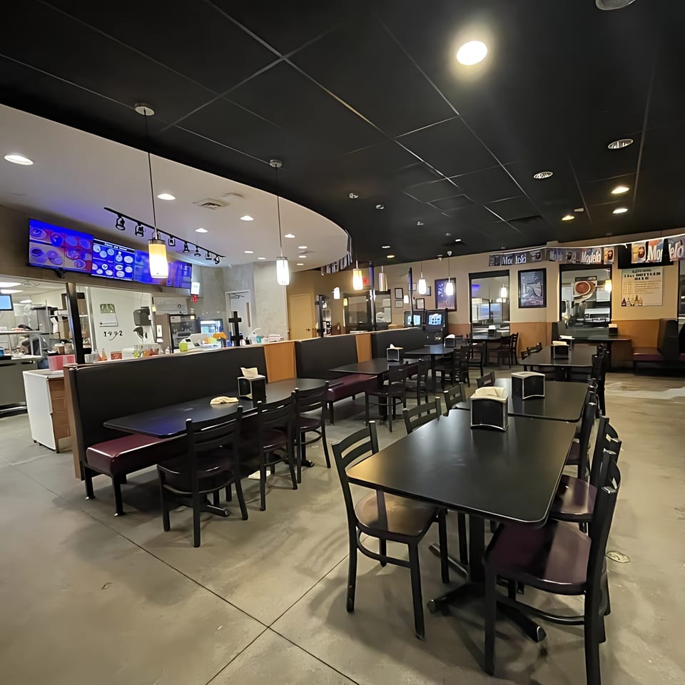 Interior of Taqueria La Flama, showing empty tables, booths, and a counter area with menu screens.