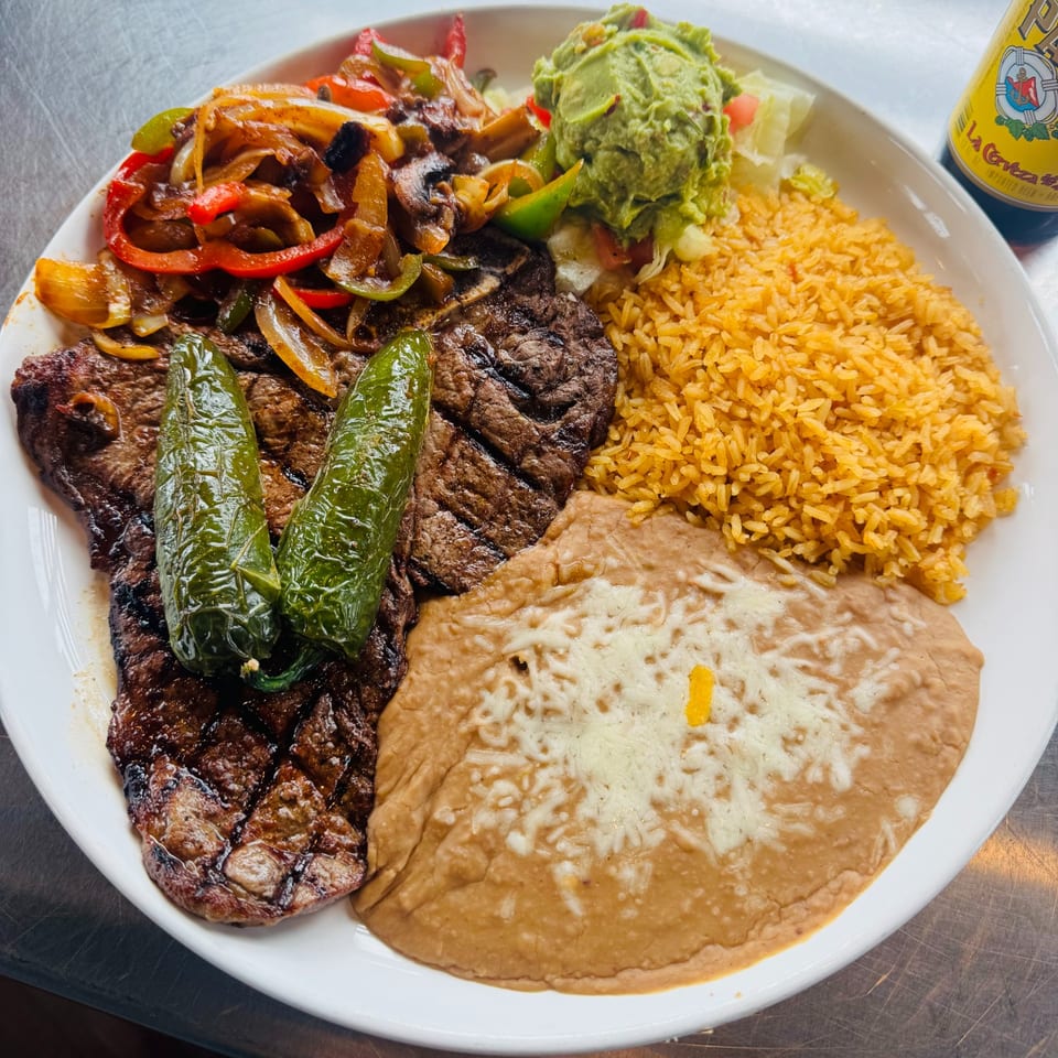 Grilled steak with two green chiles, fajita vegetables, rice, refried beans, guacamole, and salad.